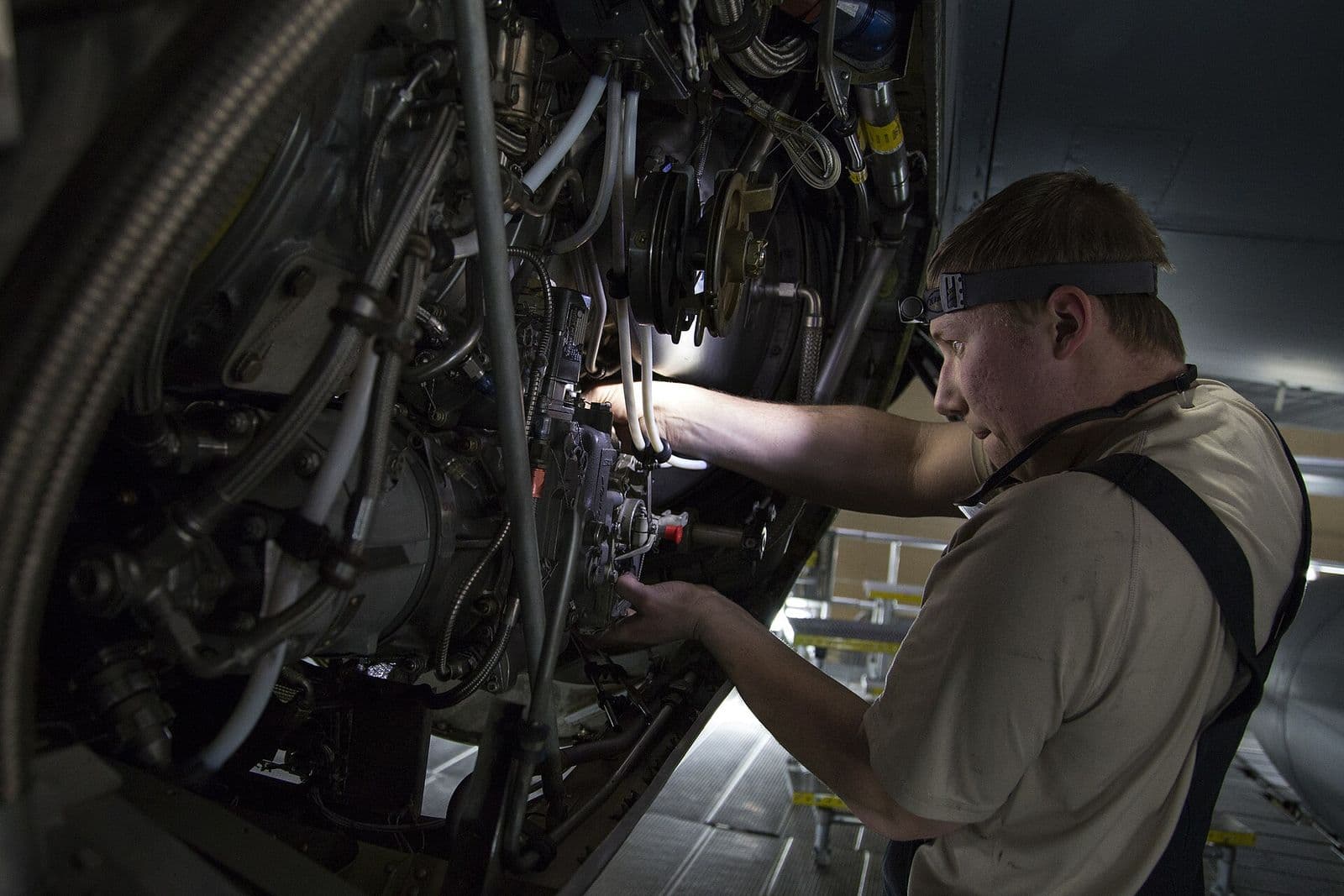A mechanic wearing a head lamp works inside the open nacelle of an HC-130 turboprop engine